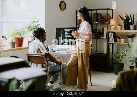 Joyful young ethnically diverse male and female colleagues chatting during coffee break at work in modern IT company office Stock Photo