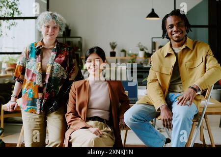 Group of three diverse gen Z colleagues wearing stylish outfits posing for camera in modern eco-friendly office Stock Photo