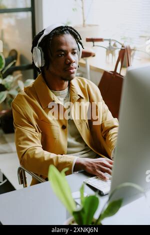 Vertical high angle view of young African American programmer wearing headphones coding on desktop computer in modern office Stock Photo