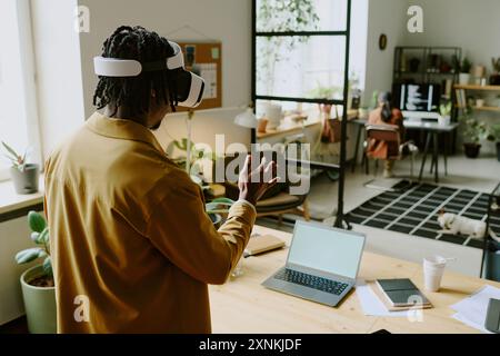 High angle view shot of young African American male programmer using VR headset at work in modern IT company office Stock Photo