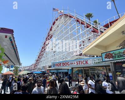 Crowds enjoying a sunny day with colorful stalls and the iconic Giant Dipper historic roller coaster in the background, Santa Cruz Beach Boardwalk, Santa Cruz, California, June 22, 2024. (Photo by Smith Collection/Gado/Sipa USA) Stock Photo