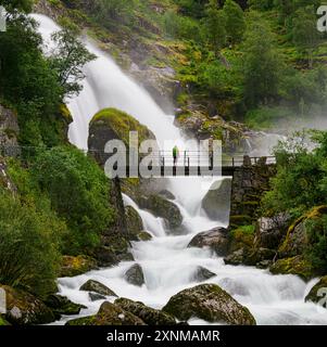 Walker on the bridge beside Kleivafossen waterfall the meltwaters of the Jostedal Glacier plunging down a steep ravine into Briksdal in central Norway Stock Photo