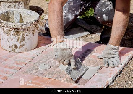 Construction worker applies adhesive to flexible faux brick panel reinforced with plastic mesh. Stock Photo
