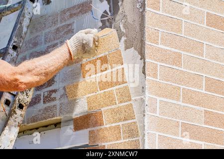 Wall facade with brick texture effect of thin brick piece, house painter smeared wall with glue and puts fake brick panel on it. Stock Photo