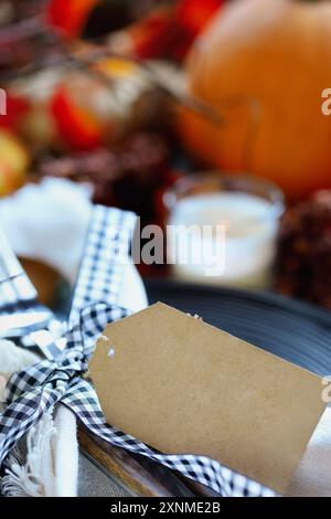 Thanksgiving place setting with blank paper card, plate, napkin, and silverware on a  decorated table. Selective focus with blurred foreground and bac Stock Photo