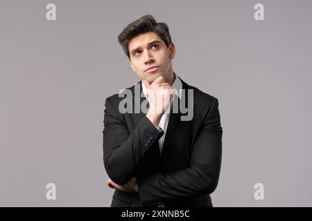 Thinking man looking up and around on grey background. Worried contemplative face expressions. Handsome male model in formal suit Stock Photo