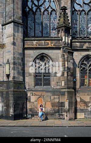 Young woman sitting reading in the sunshine in Parliament Square in Edinburgh's Old Town. Stock Photo