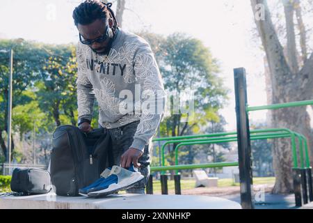 Young African Man standing in the park taking out his running shoes from his backpack for training, he is getting ready for training in the park Stock Photo