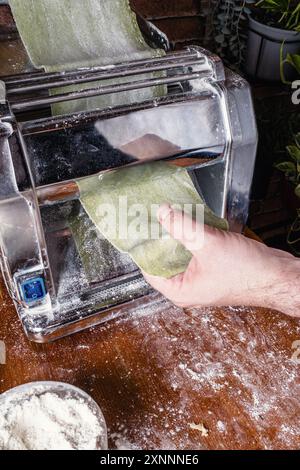 Adult hands prepare homemade pasta, rolling out the dough with a pasta machine in a restaurant kitchen. Stock Photo