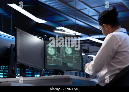Software developer using computer in server room to support global connections using their hardware. IT expert inspecting data center hardware supporting worldwide network using PC Stock Photo