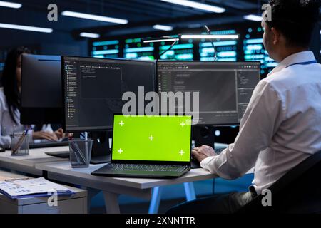 Programmers colleagues using mockup laptop to check server clusters configuration settings. Specialists checking event logs in monitoring software on green screen notebook in data center Stock Photo