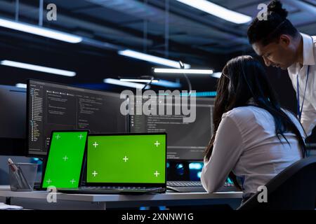 Engineers in data center using isolated screen laptop and tablet to find firewall misconfigurations affecting servers. Employees in server room checking systems bottlenecks using chroma key devices Stock Photo