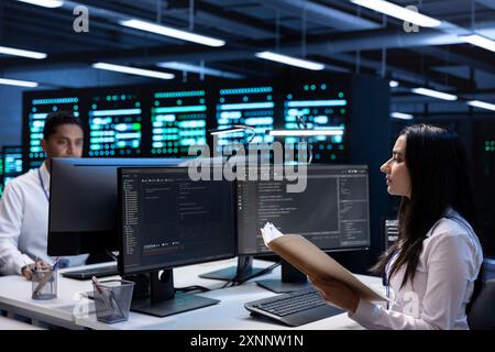 Team of engineers in data center checking emergency procedures documents to ensure system failure prevention. Colleagues in server farm workspace ensuring compliance with industry regulations Stock Photo