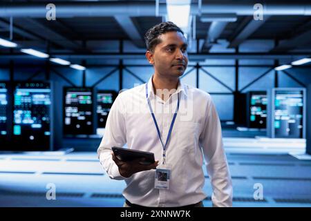Admin in server hub checking recovery plan on tablet, monitoring data center energy consumption across components, making sure sensors are functioning optimally, doing routine disk checks Stock Photo