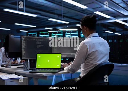 Engineer in server hub using isolated screen laptop to repair equipment storing datasets. Professional using chroma key notebook to do debugging on rigs doing computational operations Stock Photo