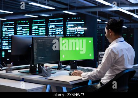 Programmer in data center using green screen computer to check for server performance issues. IT professional in server hub fixing errors slowing down hardware using mockup desktop PC Stock Photo