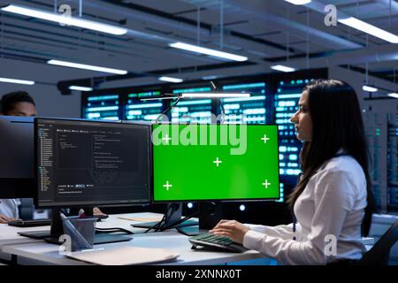 Coworkers in data center checking equipment performance on green screen computer after upgrading infrastructure. Engineers doing maintenance on supercomputers in servers room using mockup PC Stock Photo
