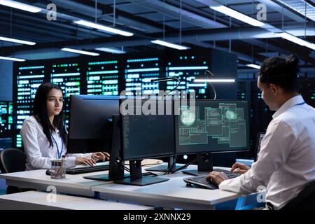 Programmers using computer in server room to support global connections using their hardware. IT professionals inspecting data center facility infrastructure supporting worldwide network Stock Photo