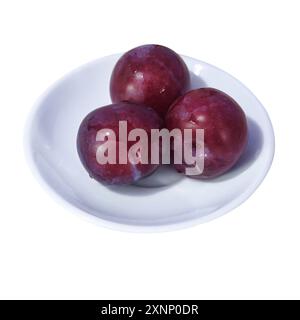 Three ripe plums on a white saucer isolate on a white background close-up. Stock Photo