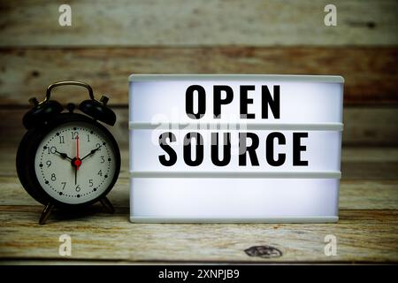 Open Source text on LED lightbox with alarm clock on wooden background Stock Photo