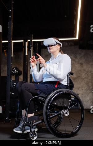 Vertical full length portrait of woman with disability using wheelchair and wearing VR headset in gym during immersive training Stock Photo