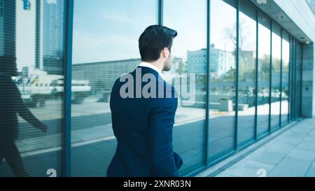 An American businessman walks inside a modern building while leaning on a glass window inside the building. Stock Photo