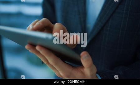 Young man holding a digital tablet in his hands and standing in a building, Successful millennial Arab businessman using a tablet while waiting Stock Photo