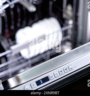 Woman's hand turns on the dishwasher to wash the dishes. Built-in appliances in the kitchen. Stock Photo