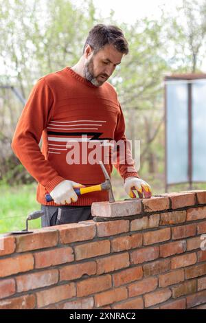 a man builds a brick wall, puts a brick on a cement-sand mortar, tapping on the brick with a construction hammer Stock Photo