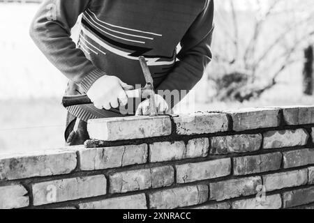 a man builds a brick wall, puts a brick on a cement-sand mortar, tapping on the brick with a construction hammer black white photo Stock Photo