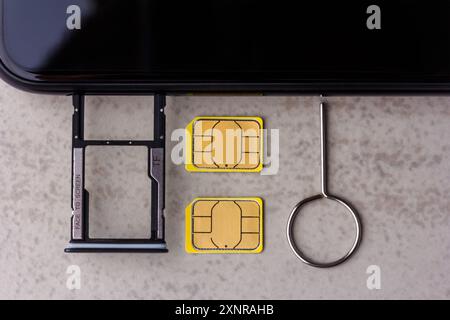 smartphone and open slots for micro SD and nano SIM cards, two nano SIM cards and metal key on grey background top view Stock Photo