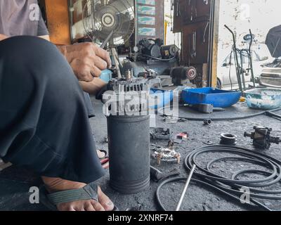Close-up of a mechanic repairing an auto part in a workshop, surrounded by various tools and mechanical components. Stock Photo