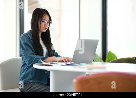A woman is sitting at a table with a laptop in front of her Stock Photo
