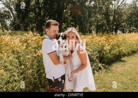 Smiling young couple with their dog in front of wildflowers Stock Photo