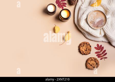 Autumn cozy composition. Cup of chocolate or coffee drink, chocolate chip cookies, burning candles and yellow autumn leaves on beige background, top v Stock Photo