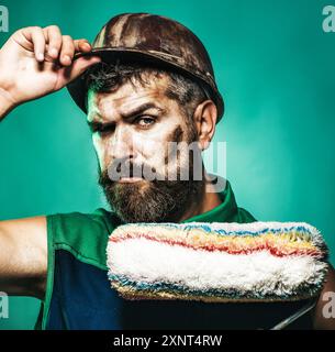 Closeup portrait of painter man with paint roller. Professional painter with painting roller. Male painter or designer in hard hat. Room painting job. Stock Photo