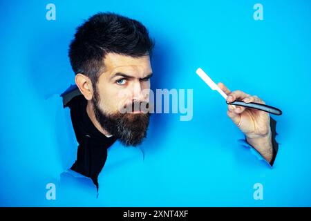 Barbershop advertising. Bearded man with straight razor looking through hole in paper. Mustache men. Male beard. Serious man with beard and mustache w Stock Photo