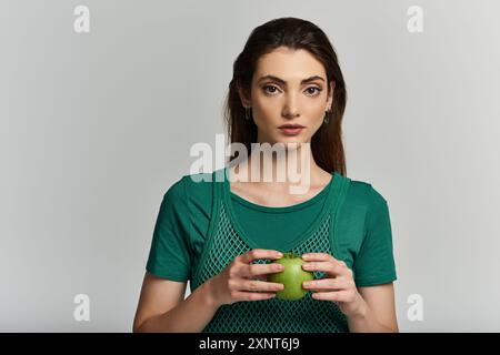 A young woman in a green outfit holds an unripe green fruit. Stock Photo