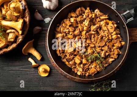 Fried chanterelle mushrooms in pan on dark wooden background, top view. Forest Mushrooms chanterelles raw and roasted, seasonal local meal. Stock Photo