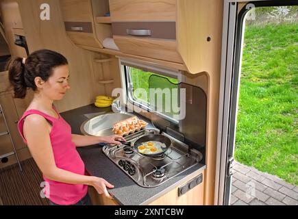 Family vacation, RV holiday trip, camping, happy smiling woman cooking in camper, motorhome interior Stock Photo