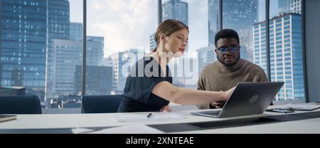 Businesspeople in Skyscraper Office: Business Meeting of Two Managers Using Laptop. Female CEO and African American Operations Director Discuss Strategy, Implementing Financial Plans. Stock Photo
