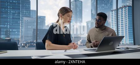 Businesspeople in Modern Office: Business Meeting of Two Managers Using Laptop. Female CEO and African American Operations Director Discuss Strategy, Implementing Financial Plans. Stock Photo