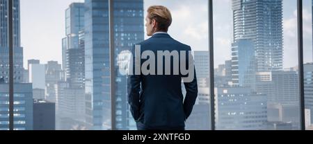 Thoughtful Young Businessman in a Perfect Tailored Suit Standing in His Modern Office Looking out of the Window on Big City with Skyscrapers. Finance Manager Planning Project Strategy. Stock Photo