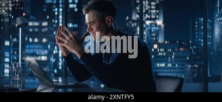 Successful Businessman Working on Laptop Computer in Big City Office Late At Night. Financial Investment Analyst Checking Data And Feeling Stressed Due To Negative Corporate Report. Stock Photo