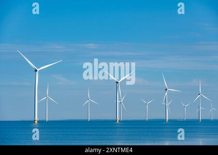 Tall windmill turbines against a clear blue sky, generating renewable energy in the serene Dutch landscape by the sea. windmill park Westermeerdijk in the Noordoostpolder Netherlands Stock Photo