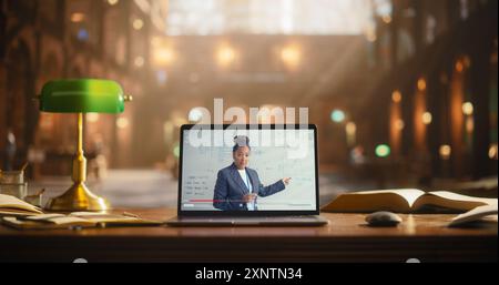 Engaging Online Presentation by a Professional Black Female on a Laptop Screen, Set in a Classic Library Environment. Books and a Green Desk Lamp Surround the Computer Displaying Educational Content. Stock Photo