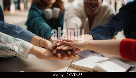 Diverse Group of Students Collaborating in a Library, Hands Joined in Unity. Multiethnic Teamwork Displayed by Young Adults Studying Together, Sharing Ideas and Supporting Each Other Academically Stock Photo