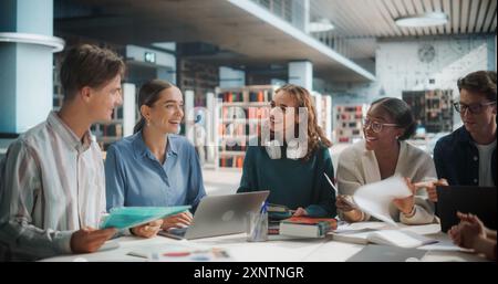 Diverse Group of Students Collaborating on a Project in a Modern Library. Young Adults Engaged in Discussion, Using Laptop and Documents, Smiling and Sharing Ideas in an Educational Setting Stock Photo