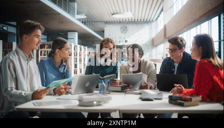 Diverse Group of Students Collaborating on a Project in a Modern Library. Young Adults Using Laptops and Books for Research, Engaged in Academic Discussion with a Focus on Technology and Education. Stock Photo