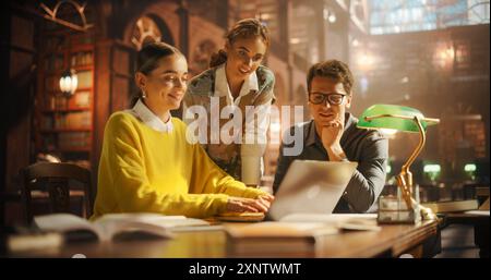 Engaged Group of Students Collaborating Over a Laptop in a Cozy Library Setting, Surrounded by Books. Two Women and One Man Discussing Academic Project, Focused and Smiling. Stock Photo